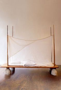 a bed that is made out of wood and white netting on top of it, sitting on some rocks