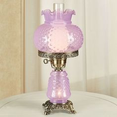 a pink glass lamp sitting on top of a white table next to a curtained window