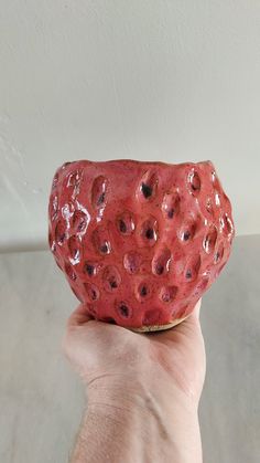 a hand holding a red ceramic bowl with holes in it