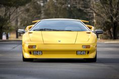 a yellow sports car is parked on the side of the road in front of some trees