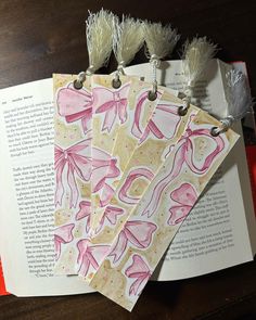 three bookmarks with pink and white designs on them sitting next to an open book