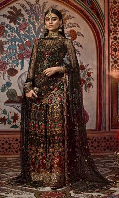 a woman in a black and gold outfit standing on a rug with an ornate wall behind her