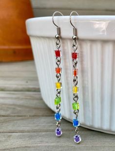 multicolored glass bead dangle earrings on a white plate with a bowl in the background