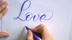 someone writing love on a piece of paper with a purple crayon pen in their left hand