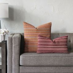 a couch with two pillows sitting on top of it next to a table and lamp