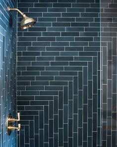 a blue tiled shower with gold faucet and hand held shower head in the corner