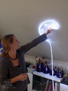 a woman is holding up a light in the shape of a circle on top of a table