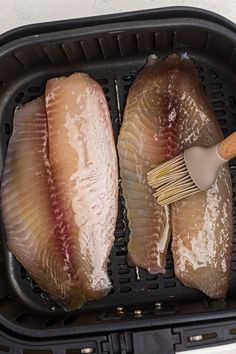 two pieces of fish are being cooked in an air fryer with a spatula