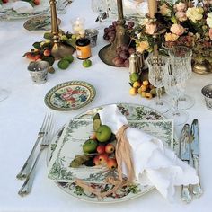 the table is set with plates, silverware and flowers in vases on it