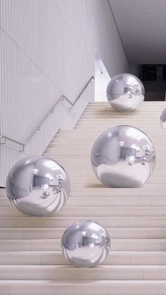 several shiny metal balls are on the steps in front of a white wall and stairs