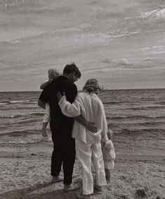 three people are standing on the beach with their arms around each other and looking out at the ocean