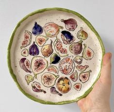 a hand holding a plate with different types of fruit painted on the inside of it