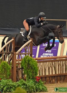 a woman riding on the back of a black horse over an obstacle at a competition