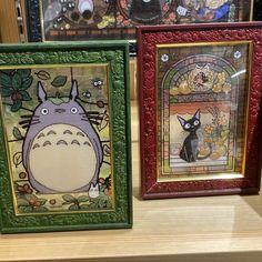 three different framed pictures on a shelf in front of some other wall hangings with cartoon characters