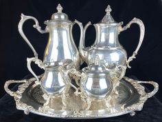 two silver tea and coffee service pieces on a metal tray with black velvet back ground