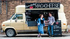 a man and woman standing in front of a food truck with an american flag painted on it