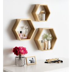 three hexagonal shelves on the wall above a desk with flowers and other items