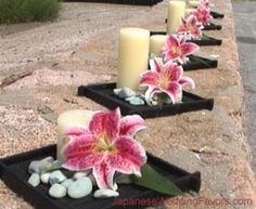 there are many candles and flowers on the side of the road that is lined with rocks