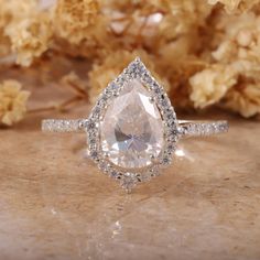 an engagement ring with a pear shaped cut diamond surrounded by small white diamonds on a marble surface