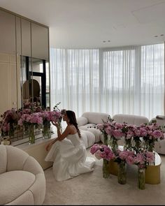 a woman kneeling in front of a mirror next to vases filled with pink flowers