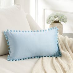 a blue pillow with pom - poms sitting on top of a white bed