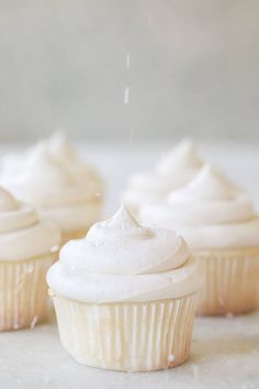 cupcakes with white frosting and sprinkles sitting on a table