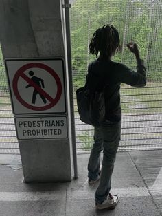 a person with dreadlocks standing in front of a no pedestrian sign and gate