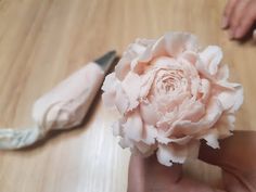 a person holding a flower in their hand with a pair of scissors on the table