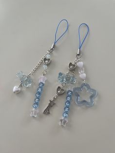 two blue and white charms are attached to silver chains on a gray surface with beads