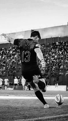 a black and white photo of a soccer player kicking the ball in front of an audience