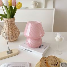 a pink vase sitting on top of a table next to a book and some bread