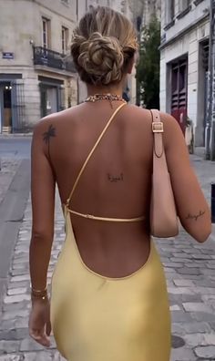 a woman in a yellow dress walking down the street with her back to the camera