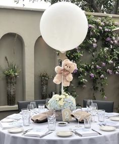 the table is set up for a party with balloons and flowers on it, including a teddy bear