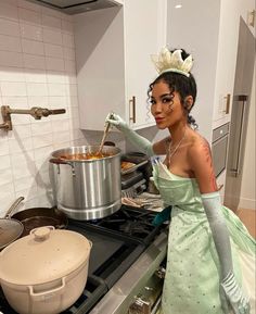 a woman in a green dress is cooking on the stove with a large pot behind her