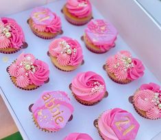 cupcakes with pink frosting and gold decorations in a white box on top of a table