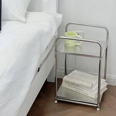 a stack of books sitting on top of a metal shelf next to a white bed