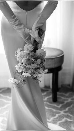 black and white photograph of woman in wedding dress holding bouquet with gloves on her back