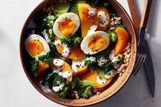 a bowl filled with broccoli, hard boiled eggs and carrots next to a fork