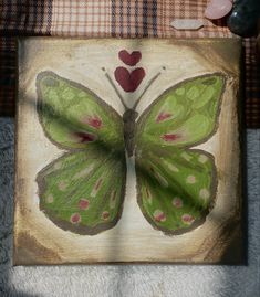 a green butterfly sitting on top of a piece of wood next to a red heart