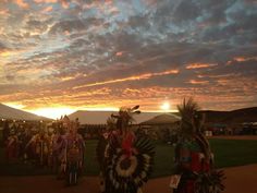 the sun is setting behind some native americans in their traditional clothing and headdress