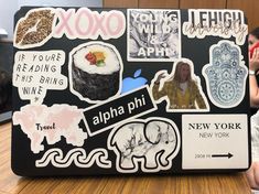 a laptop covered in stickers sitting on top of a wooden table next to a woman