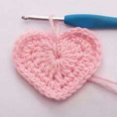 a crocheted heart is being worked on by a blue handled knitting needle with a hook in the middle