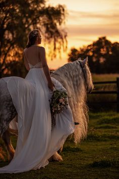 a woman in a wedding dress riding on the back of a white horse at sunset