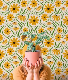 a woman covering her face with a potted plant in front of a colorful wallpaper