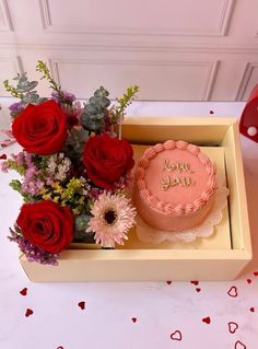 a pink cake sitting on top of a table next to red roses and other flowers