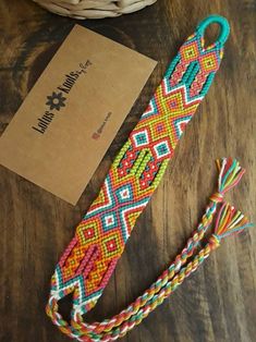 a colorful bracelet sitting on top of a wooden table next to a box and string