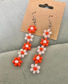 an orange and white beaded earring on a gray surface next to a pair of earrings