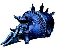 a blue metal animal head with spikes on it's face and teeth, against a white background