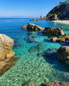 the water is crystal blue and clear with rocks on both sides, along with some cliffs in the background