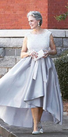 an older woman is walking down the street wearing a gray dress with a bow at the waist